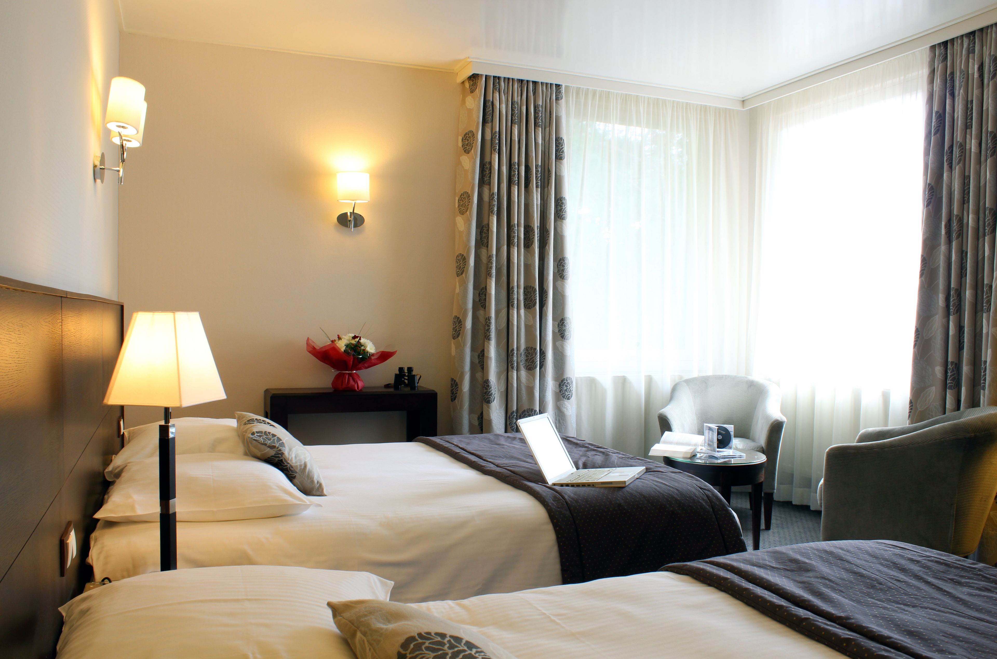 Una habitación de hotel con dos camas, un escritorio con una computadora portátil, una silla y una lámpara.