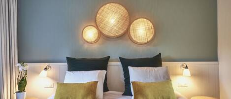 Un lit bien fait, avec des oreillers blancs et verts, une couverture bleue et un luminaire fixé au mur au-dessus.