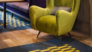 Una habitación con un sillón verde, un sofá morado y un panel de pared de madera.