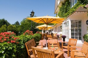 Un espace extérieur aménagé avec des tables et des chaises en bois, des parasols jaunes et un bâtiment blanc doté de grandes fenêtres.