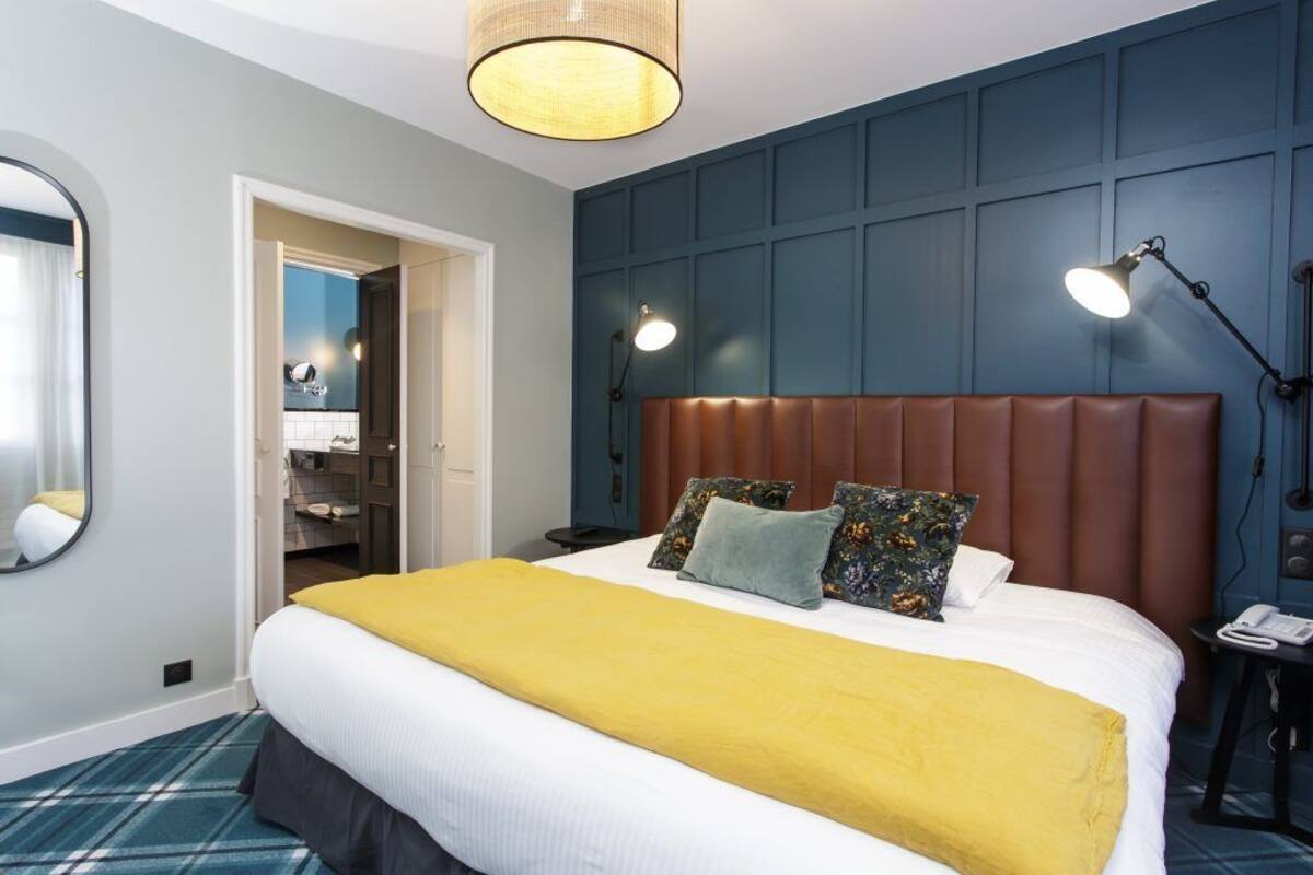Ein Hotelzimmer mit einem großen Bett, einem Spiegel, einer Nachttischlampe und einer Tür zu einem Badezimmer.