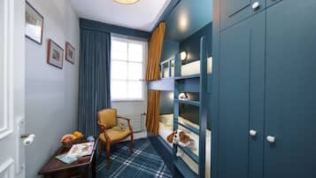 Une chambre avec un lit superposé, une chaise, une petite table avec des livres et des fruits, et une fenêtre avec des rideaux.