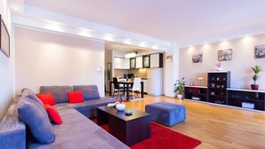 A modern living room with a grey sectional sofa, a red rug, and a dining area with a kitchen in the background. - Urban Premium Apartments - Adults Only (Porec)