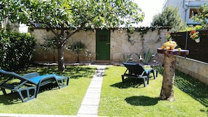 A garden with a stone wall, a green door, and two lounge chairs.