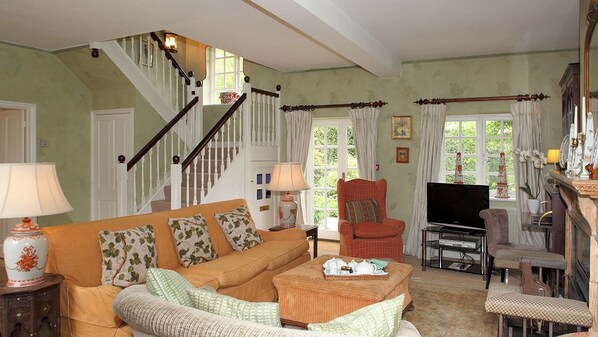 A cozy living room with a staircase, a television, and comfortable seating. - Aintree Cottage (Chipping Norton)