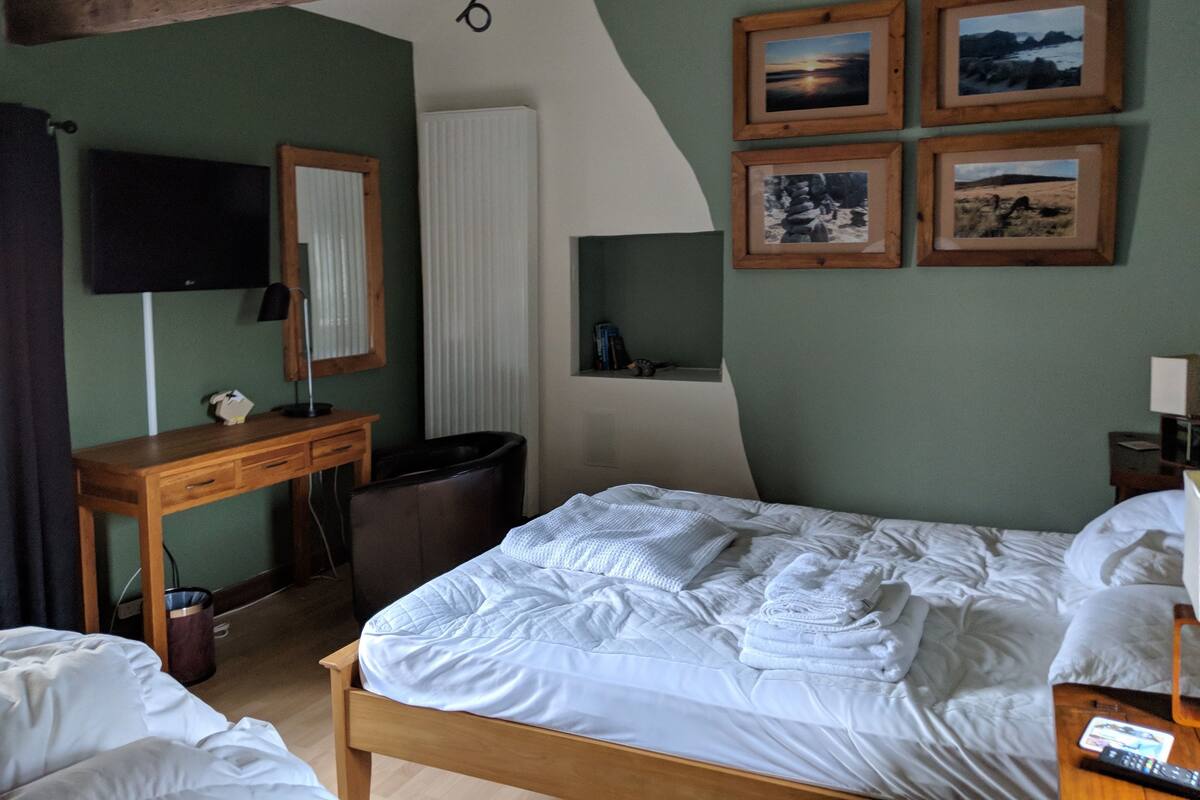 A hotel room with a bed, a desk, a chair, a TV, and framed pictures on the wall.