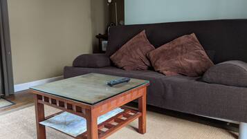 A living room with a wooden coffee table, a brown sofa with cushions, and a framed picture on the wall.