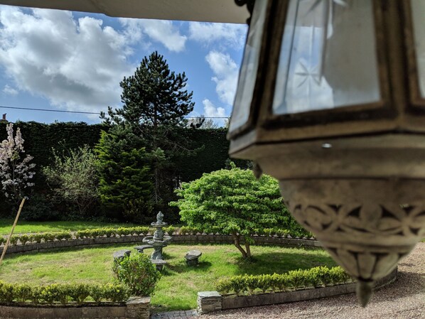 Un jardin agrémenté d’une fontaine en pierre, de haies soigneusement taillées et de différentes espèces d’arbres.