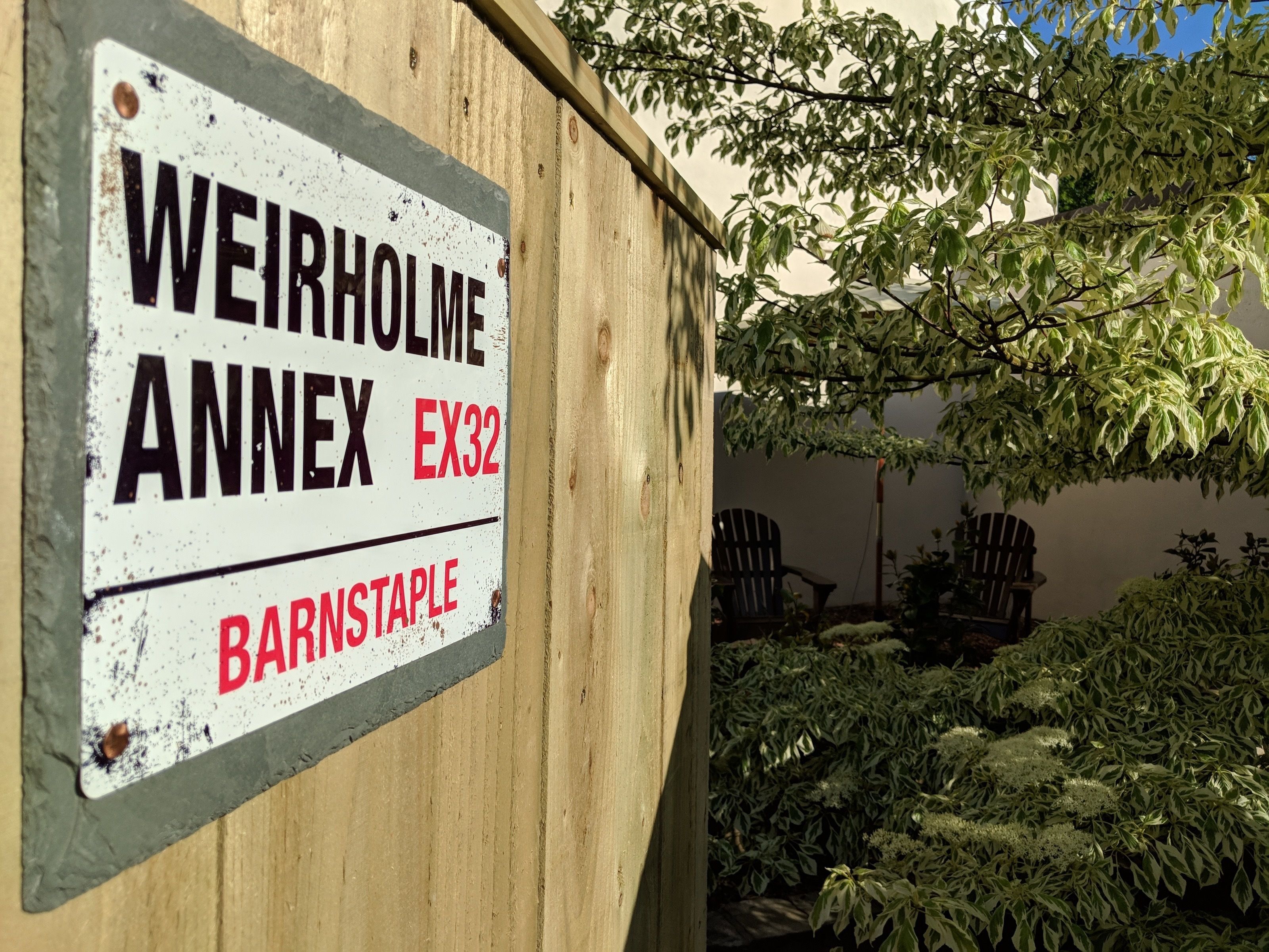 Un letrero con el texto "WEIRHOLME ANNEX EX32" y "BARNSTAPLE" en una estructura de madera.