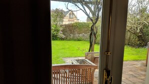 A view through a door into a courtyard with a stone pathway, wooden benches, and a stone wall. - Weirholme Annex (Barnstaple)