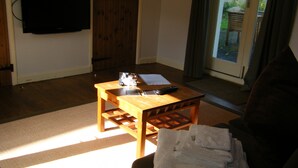 A living room with a wooden coffee table, a television mounted on the wall, and a door leading outside. - Weirholme Annex (Barnstaple)