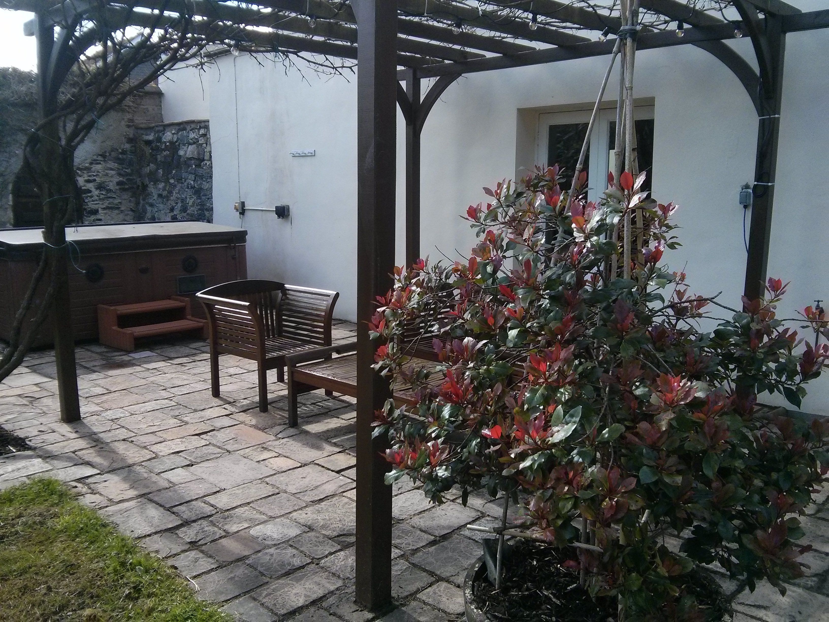 A patio area with a wooden bench, a small table, and a potted plant.