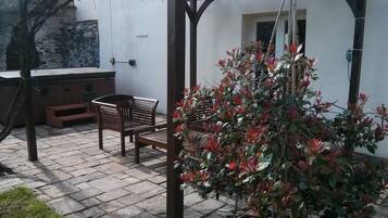 A patio area with a wooden bench, a small table, and a potted plant.