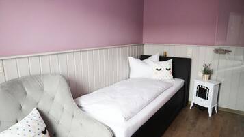 A bedroom with a bed, a chair, a small white heater, and a wall-mounted shelf.