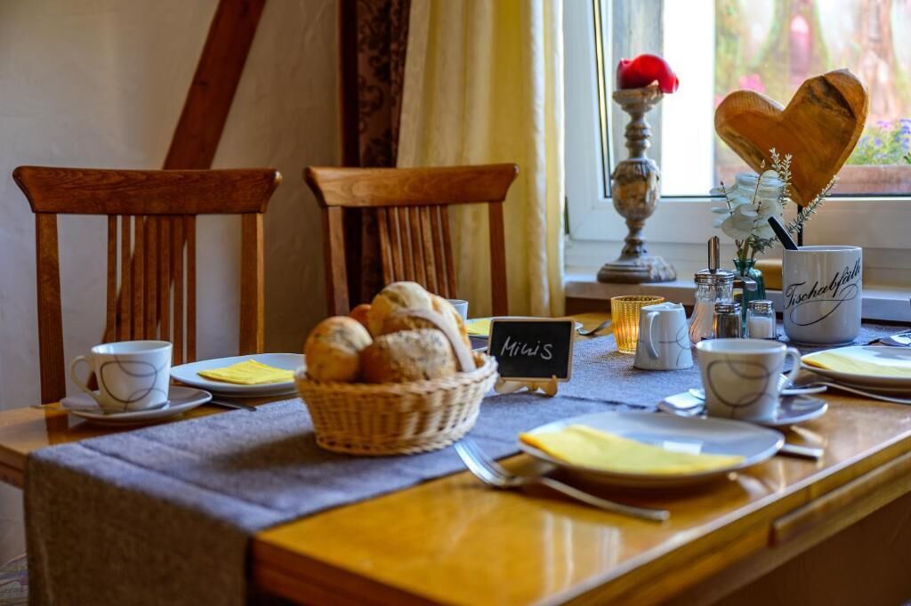 A breakfast setup with a table set for two, including bread, cups, and a sign reading 'Mies'.