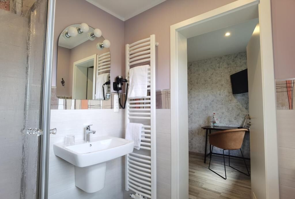 A bathroom with a sink, mirror, towel rack, and shower.