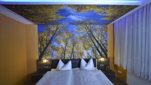 Une chambre avec un grand lit, une fresque représentant des arbres peinte au plafond et une fenêtre avec des rideaux.