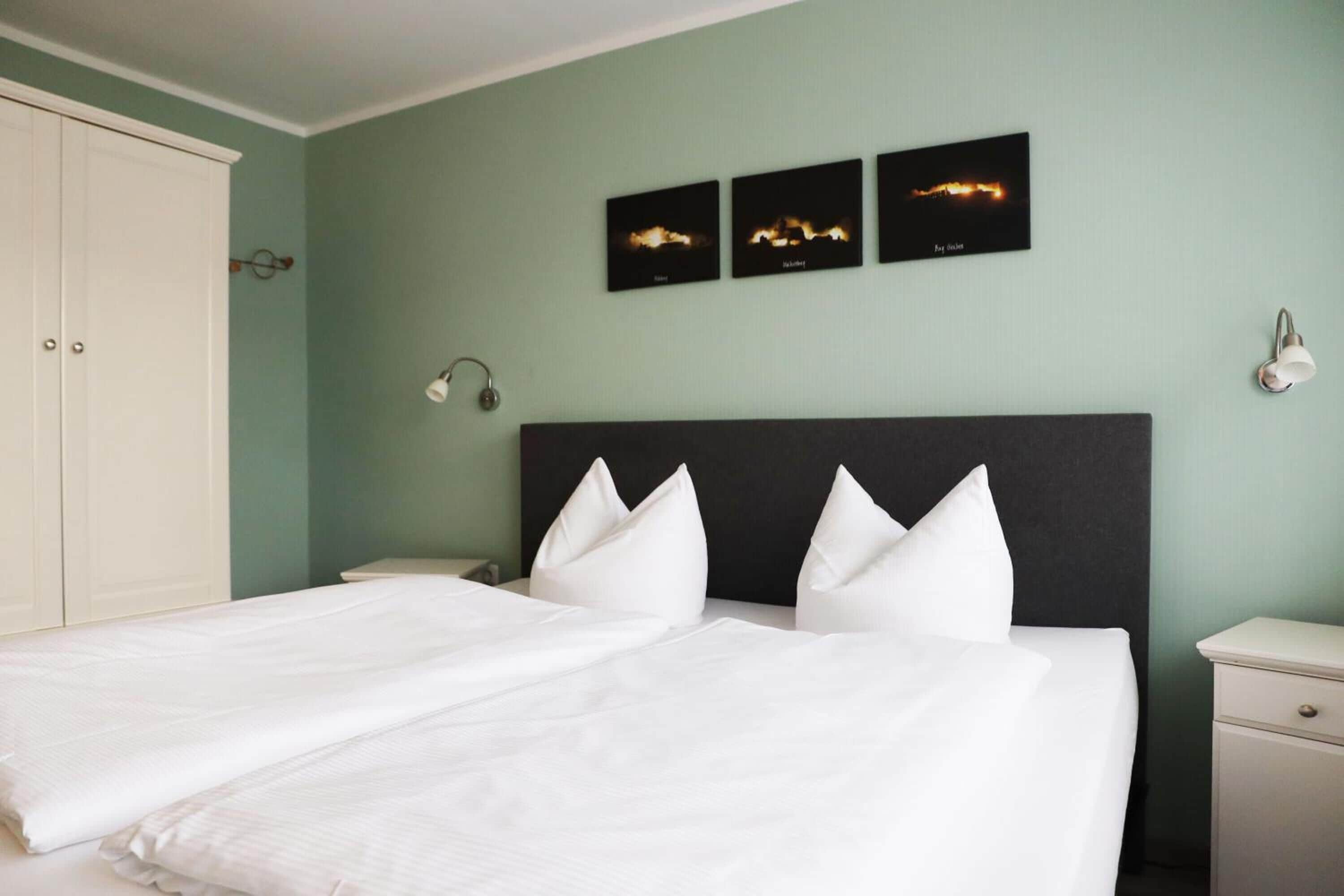 Ein Schlafzimmer mit einem großen Bett, weißer Bettwäsche, einem dunklen Kopfteil und drei gerahmten Bildern an der Wand.