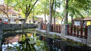 Un pont de pierre enjambant une étendue d’eau paisible, entouré d’arbres et de bâtiments traditionnels.