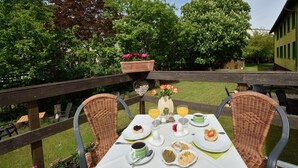 Un espace extérieur aménagé pour prendre les repas, avec des chaises en osier et une table dressée pour le petit-déjeuner.