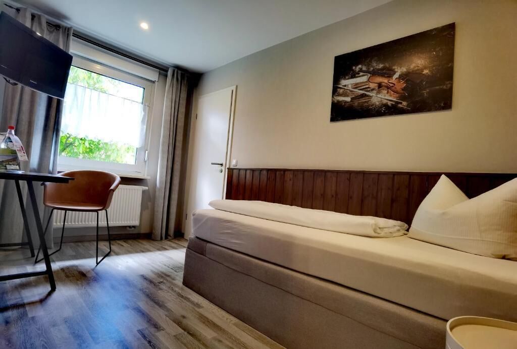 Une chambre d’hôtel avec un lit, une chaise, un bureau, une fenêtre et un tableau au mur.