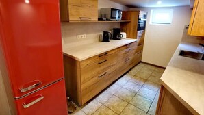 Cocina compacta con refrigerador rojo, armarios de madera, microondas y cafetera.