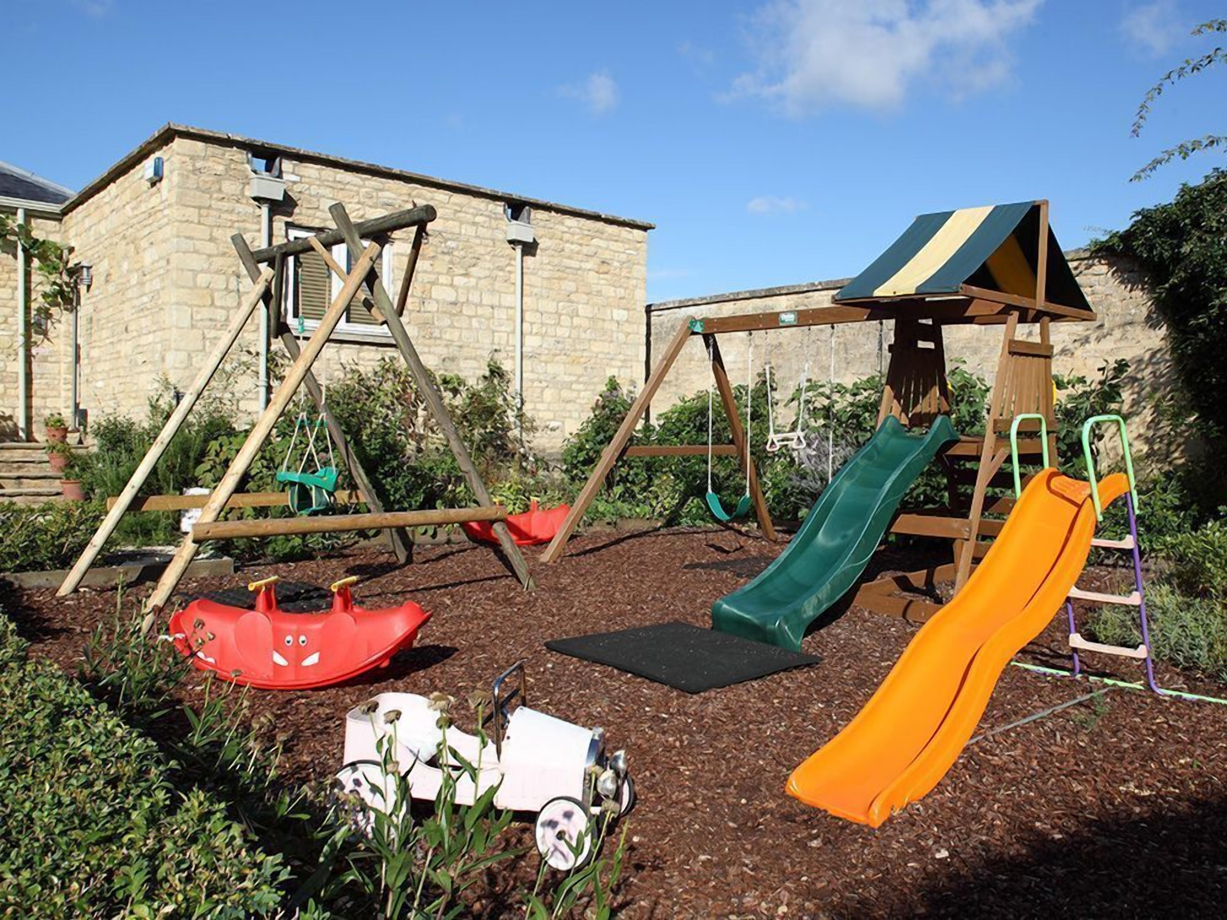 Un parque infantil con columpios, toboganes y un pequeño coche de juguete.