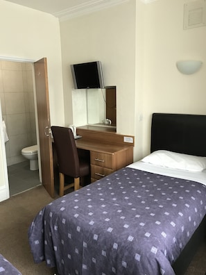 Una habitación de hotel con cama, escritorio, silla, televisión y un inodoro.