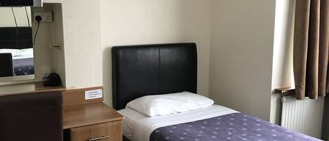Ein Hotelzimmer mit Bett, Schreibtisch, Stuhl, Fernseher und Wandleuchte.