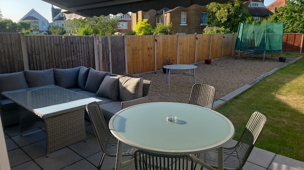 An outdoor patio with a sectional sofa, round table, and chairs. - Warwick Lodge (Surbiton)