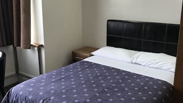 A hotel room with a bed, a nightstand, a lamp, and a window with curtains.