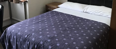 A hotel room with a bed, a nightstand, a lamp, and a window with curtains.
