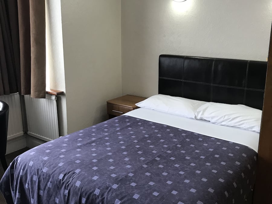 A hotel room with a bed, a nightstand, a lamp, and a window with curtains.