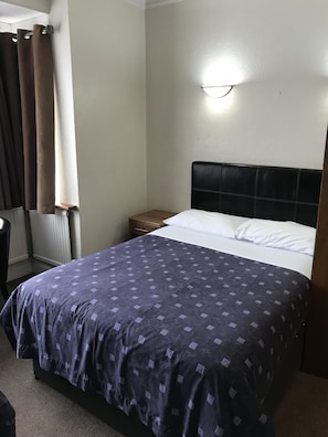 Una habitación de hotel con una cama, una mesita de noche, una lámpara y una ventana con cortinas.