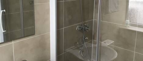 Un baño moderno con ducha de vidrio, lavamanos blanco y espejo.