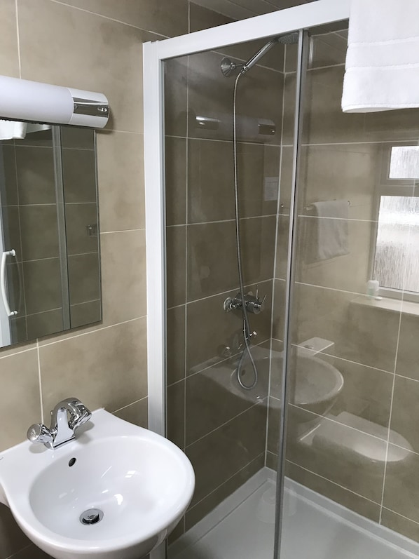 Un baño moderno con ducha de vidrio, lavamanos blanco y espejo.