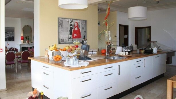 Une cuisine moderne dotée d’un îlot central, de meubles blancs et d’un coin repas visible au fond.