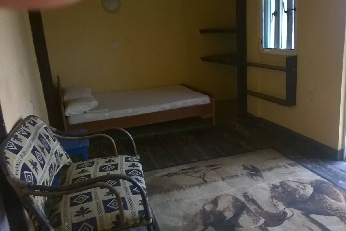 Una habitación pequeña con una cama, un sillón estampado, una ventana y un radiador.