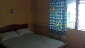 A bedroom with a bed, a nightstand, a window with a floral curtain, and a tiled floor. - Rising Phoenix Magic Beach Resort (Accra)