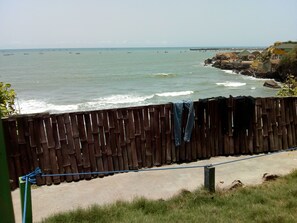 A coastal view with a wooden fence, a concrete path, and a rocky shoreline.