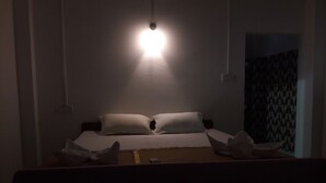 Hämärästi valaistu hotellihuone, jossa on yksi sänky, valkoiset vuodevaatteet ja yöpöytä, jossa on lamppu.