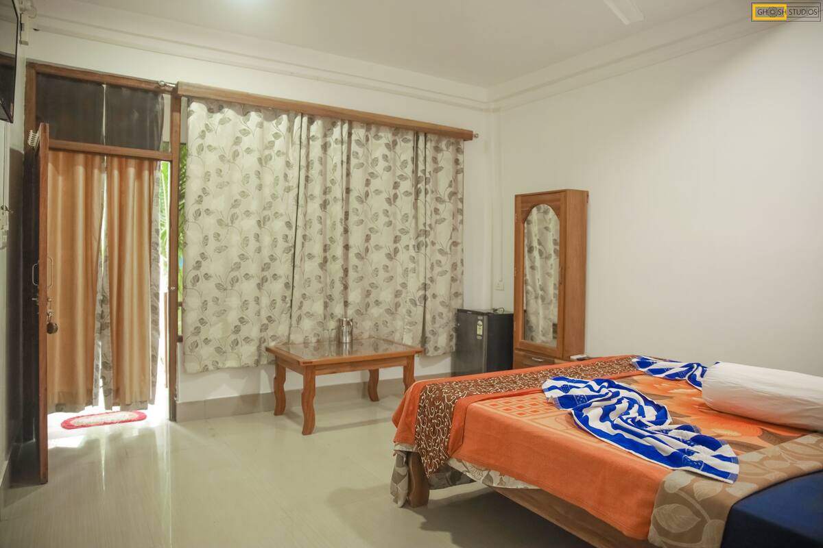 A bedroom with a bed, a wooden table, a mirror, and a sliding door leading to an outdoor area.