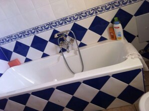 A bathroom with a white bathtub, blue and white checkered tiles, and a shower with a faucet.