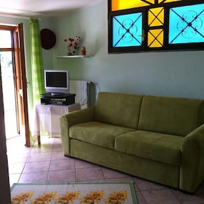 A living room with a green sofa, a television on a stand, a small table, and a window with decorative glass panes. - Villa Cerasiello (Bracigliano)