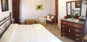 A bedroom with a bed, a dresser, a chair, a small table, and a wall with pictures.