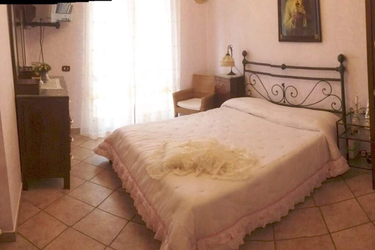 Een slaapkamer met een bed, een stoel, een kapstok, een spiegel en een radiator.