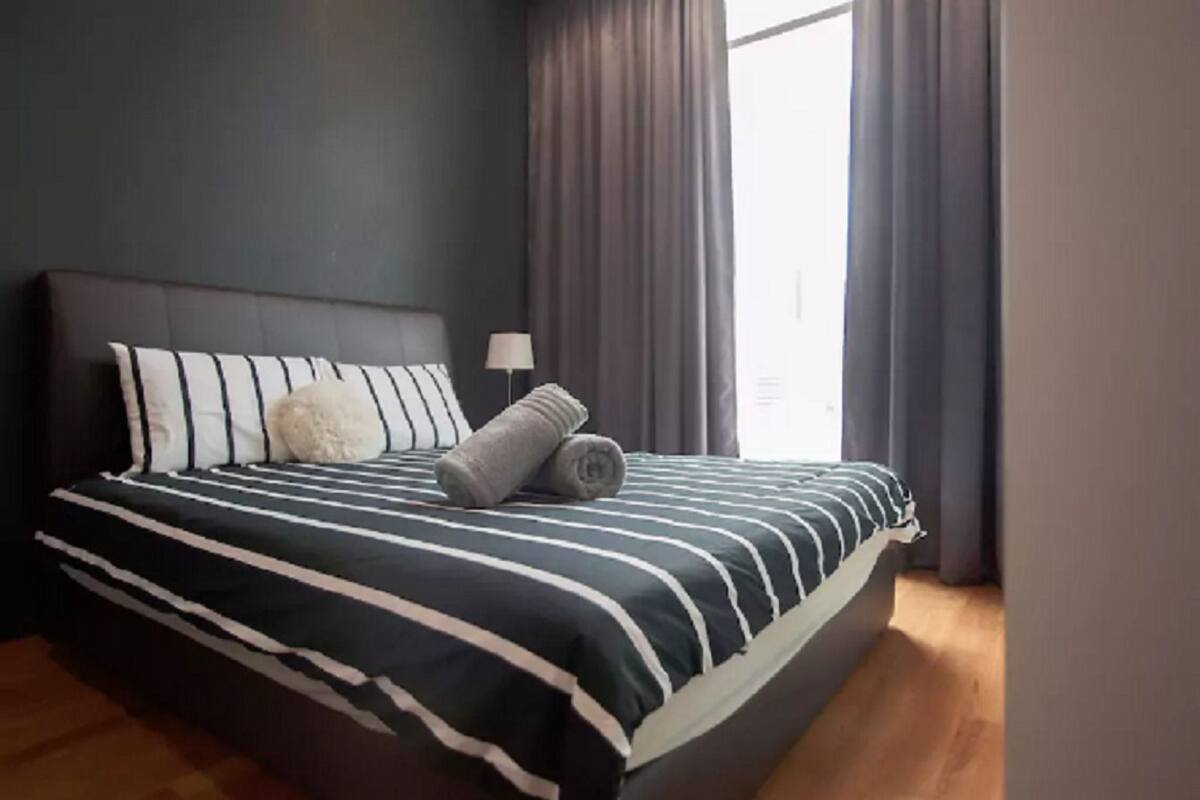 Een net opgemaakt bed met gestreept beddengoed, een zacht kussen en opgerolde handdoeken.