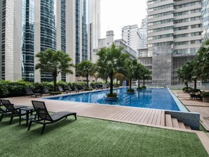 A swimming pool with lounge chairs and palm trees, surrounded by high-rise buildings. - KL101 Service Suite at Soho Suites KLCC (Kuala Lumpur)