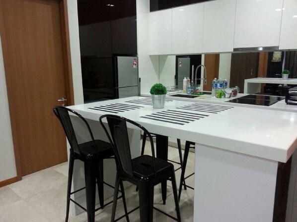 A modern kitchen with a white countertop, black chairs, and a small potted plant. - KL101 Service Suite at Soho Suites KLCC (Kuala Lumpur)