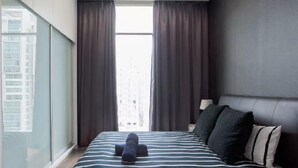A modern hotel room with a large bed, dark curtains, a view of the city, and a cityscape visible through the window.